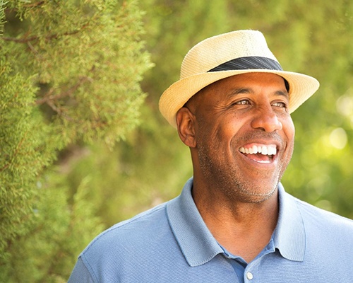 man in blue shirt and fedora smiling among trees