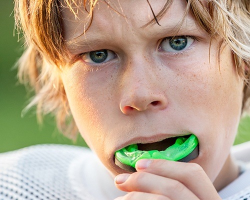 Teen boy placing green sports mouthguard