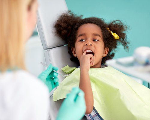 Little girl in dental chair pointing to her smile