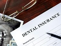 A dental insurance form, glasses, and dental X-rays on a brown wooden table