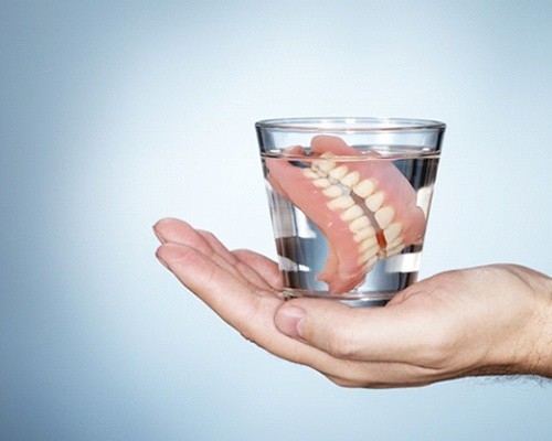 hand holding dentures in glass of water 