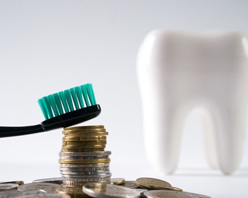 Pila de monedas con cepillo de dientes y un diente