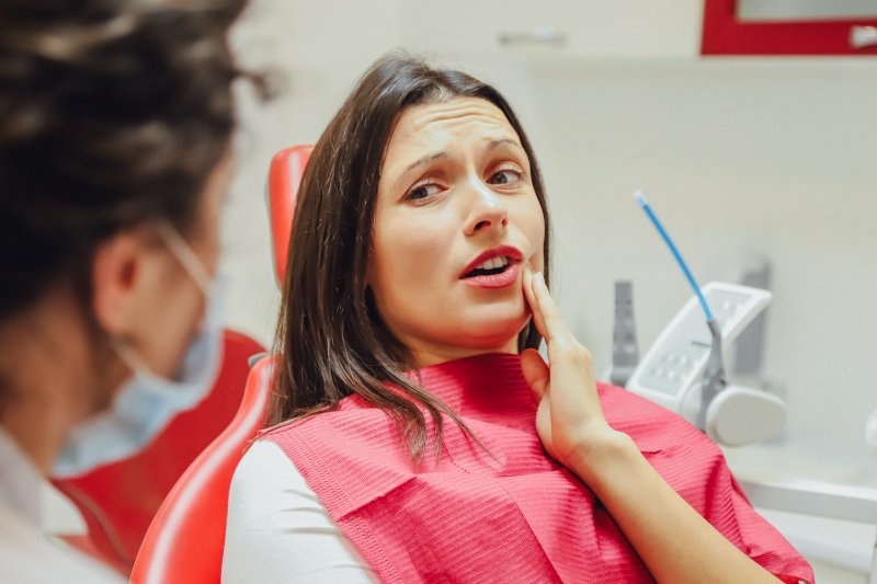 A young woman holding her cheek in pain while listening to her dentist