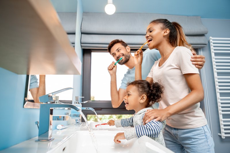 Parents and their daughter brushing their teeth in front of the mirror at home