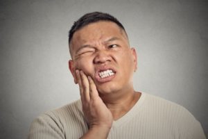 Pained man with hand on cheek needs to visit emergency dentist center