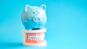 light blue piggy bank sitting atop false teeth against light blue background 