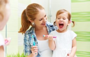 mother teaching her daughter how to brush her teeth
