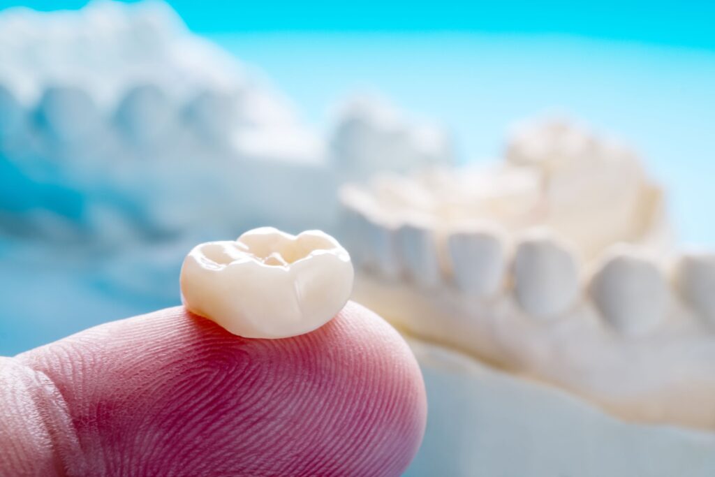 Dental crown on fingertip with light blue background
